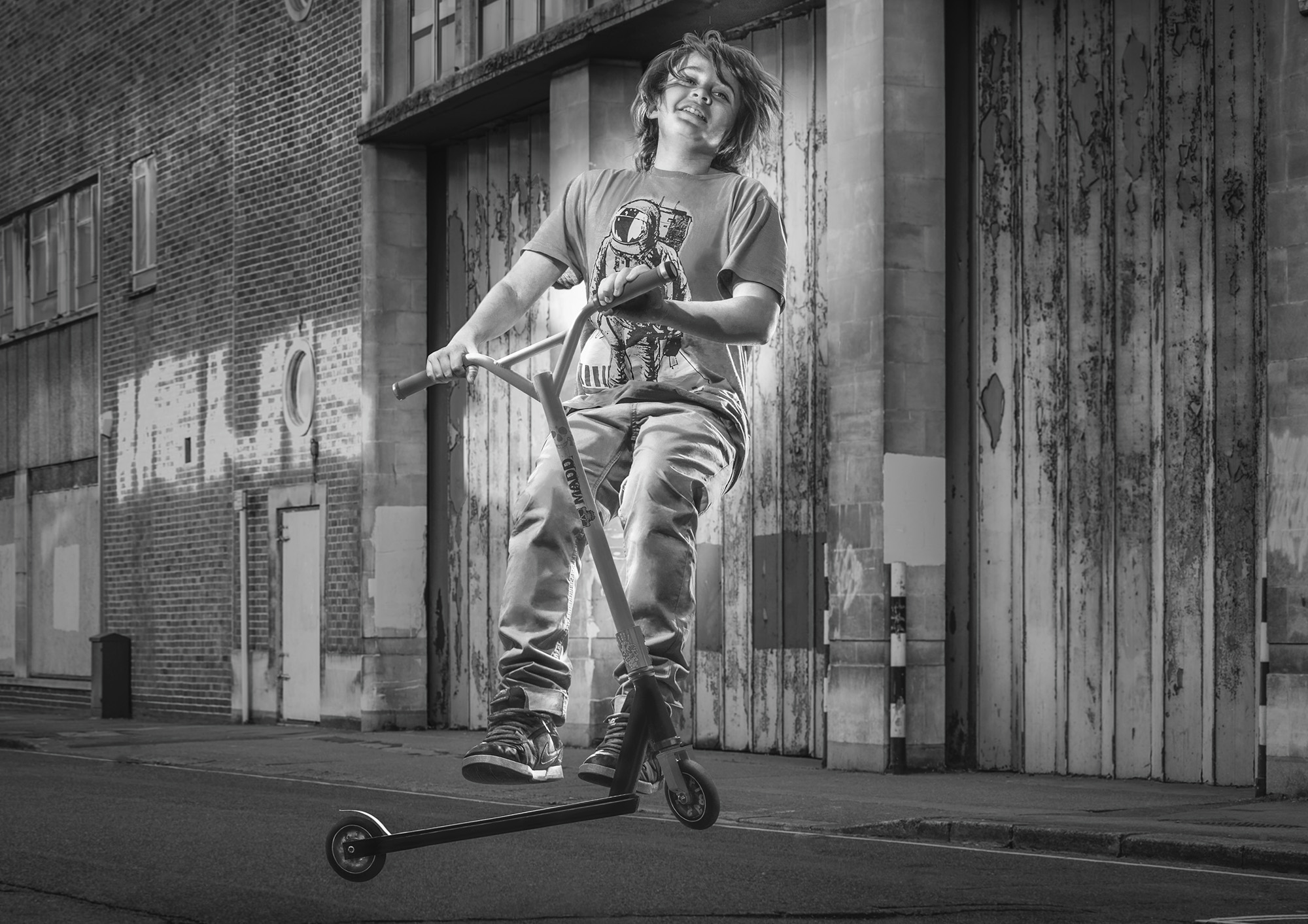 B/W photograph of boy in mid air spin on a push scooter